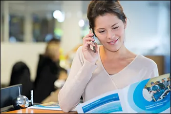 Photo of woman looking at printed brochure while talking on telephone